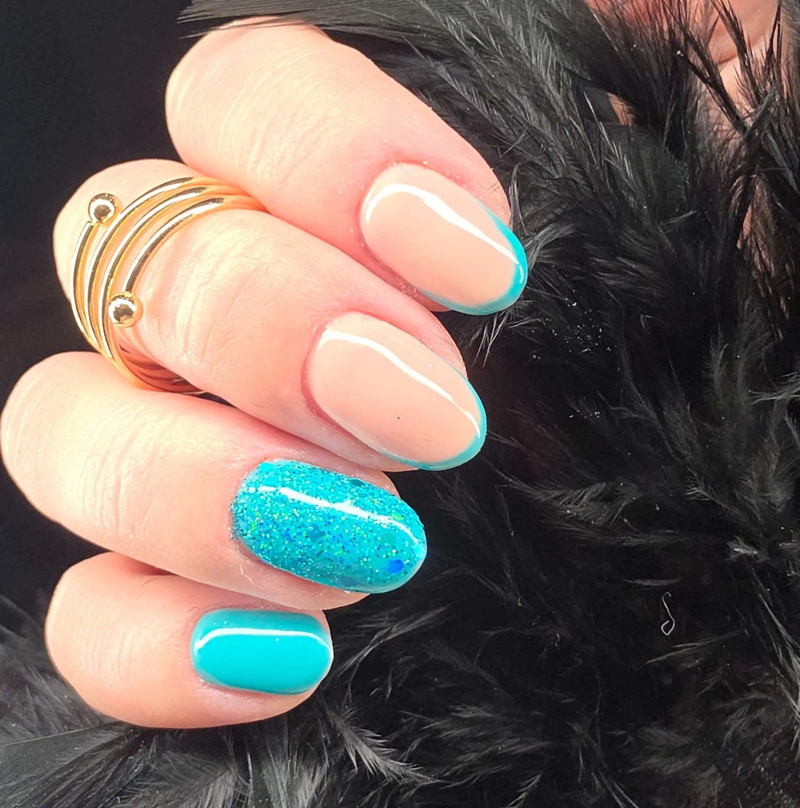 Nude nails with turquoise tips and a turquoise glitter accent on black feathers