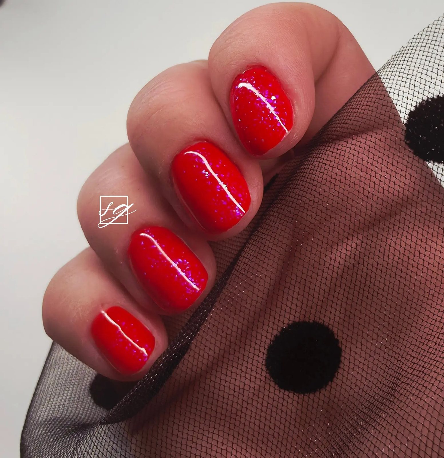 Glossy red glitter gel nails against black polka dot tulle