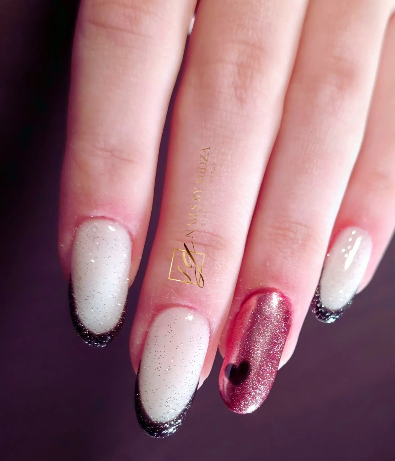 Milky glitter almond nails with black glitter French tips and a pink cat-eye accent nail with a heart