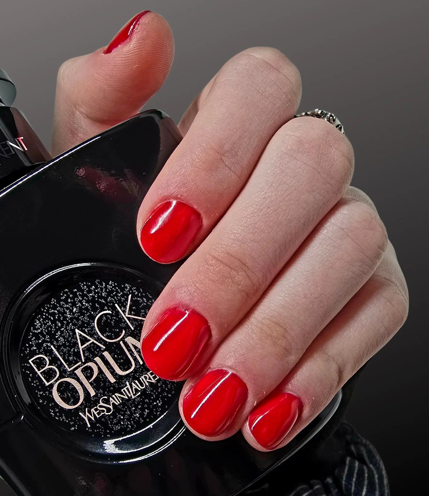 Bright red glossy nails holding a black perfume bottle